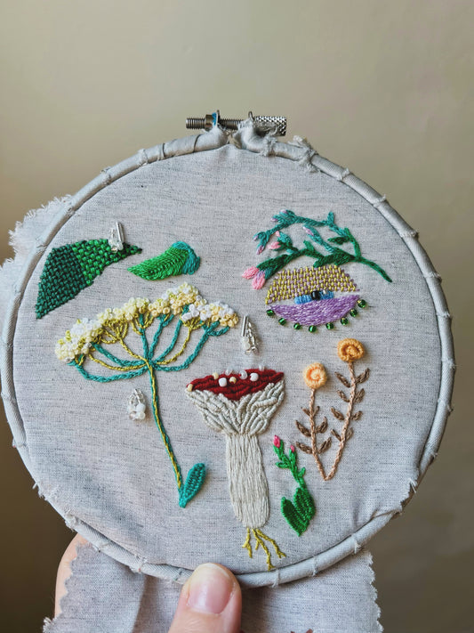 Embroidery hoop with mushroom and wildflowers-themed design on a neutral background