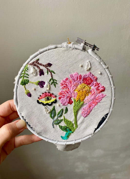 Embroidery hoop with wild rose held by a hand against a neutral background