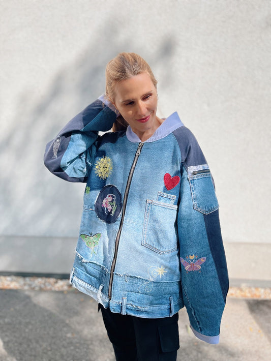 Patchwork blue denim bomber jacket with colourful embroidery, reused jeans pockets and a front zip.