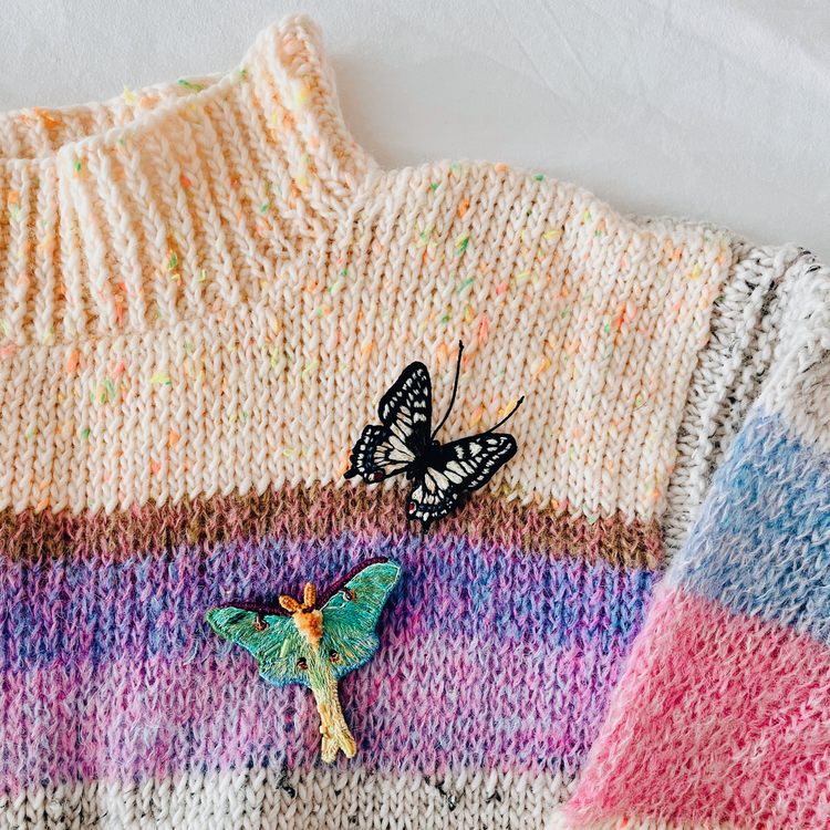 Woman wearing handmade embroidered brooches on blue jeans jacket while sitting on the beach