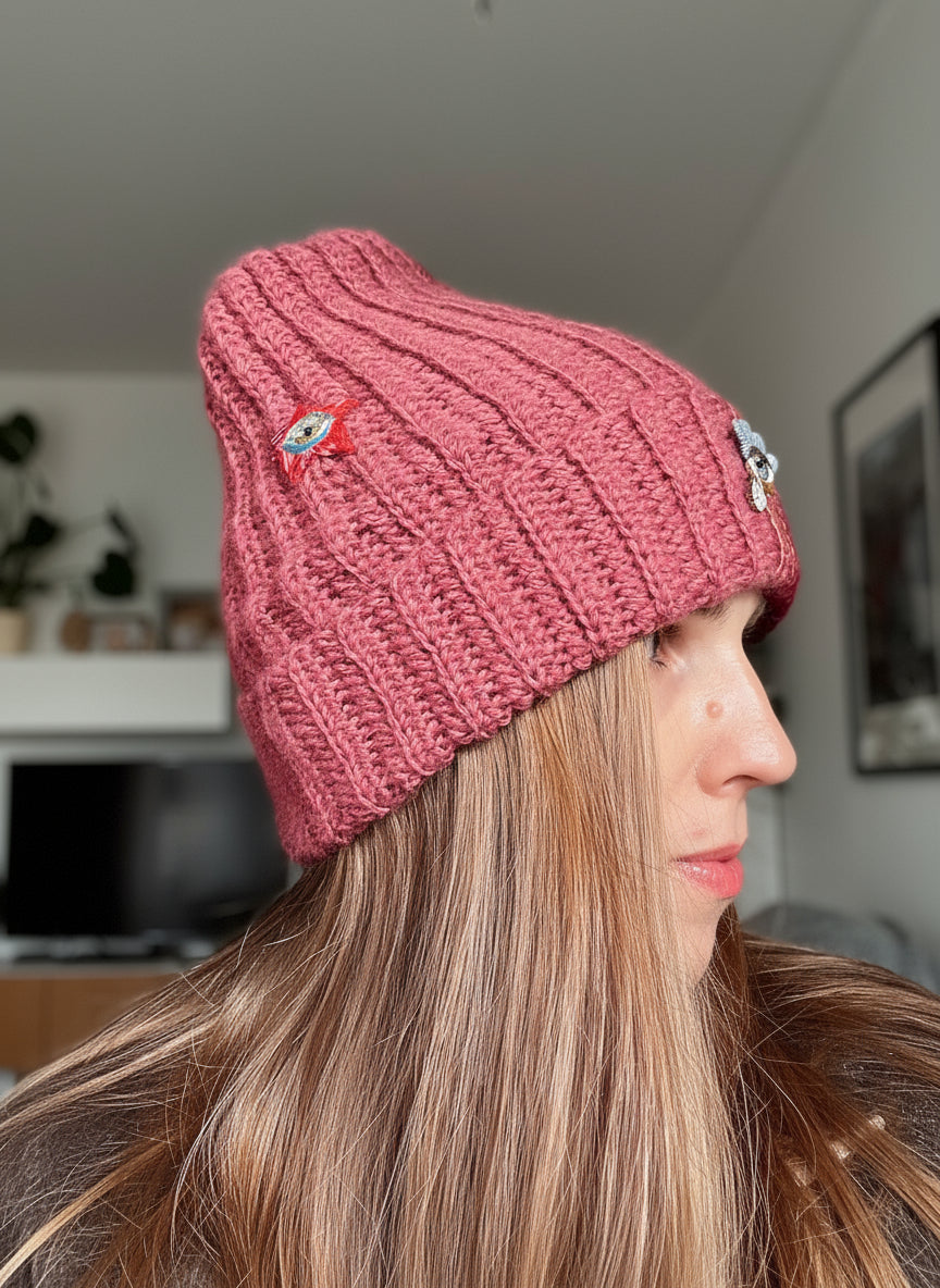 Person wearing a pink knitted beanie with decorative elements indoors.