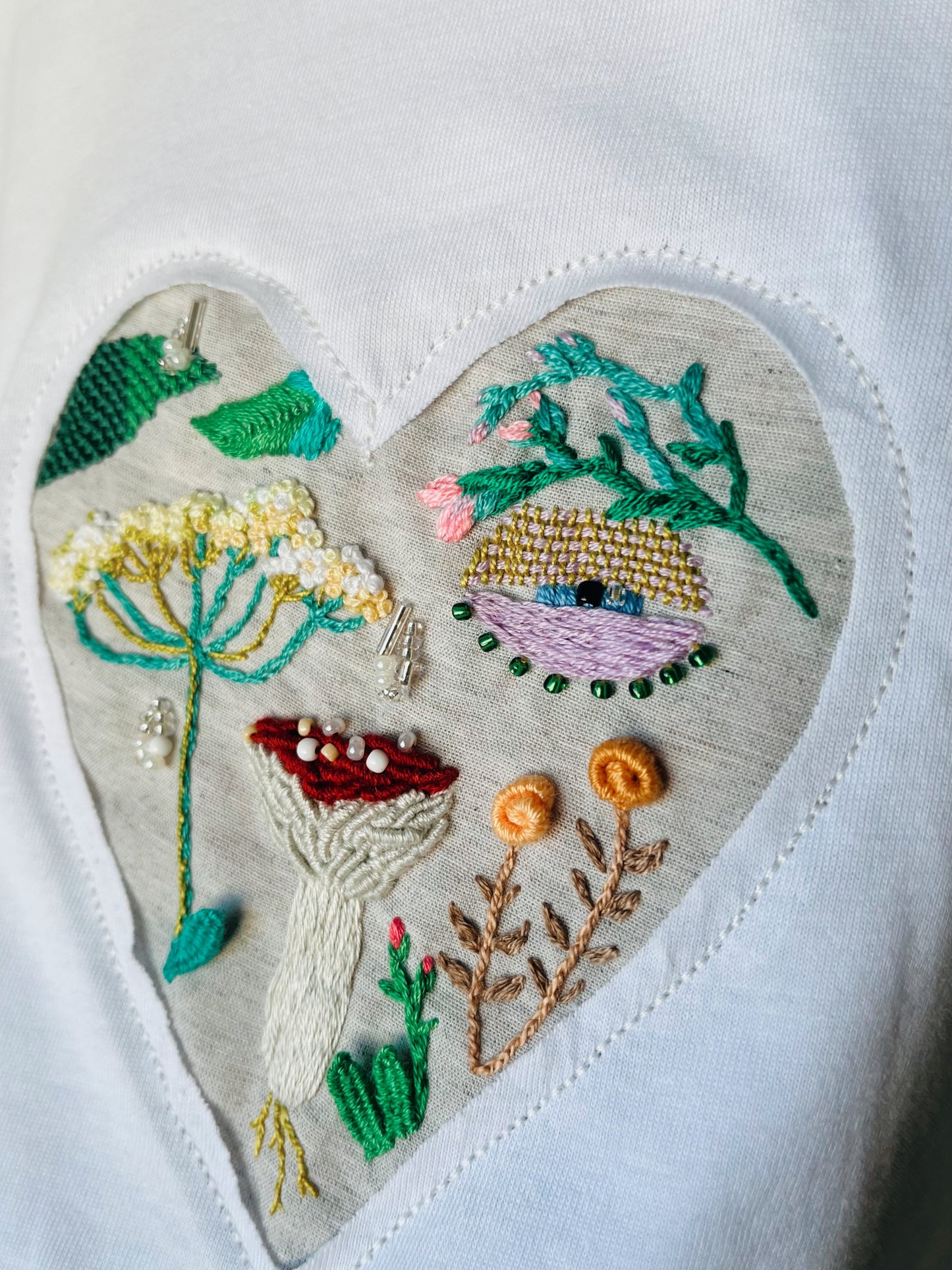 A close up of a white t-shirt with embroidered heart featuring mushroom and wildflowers