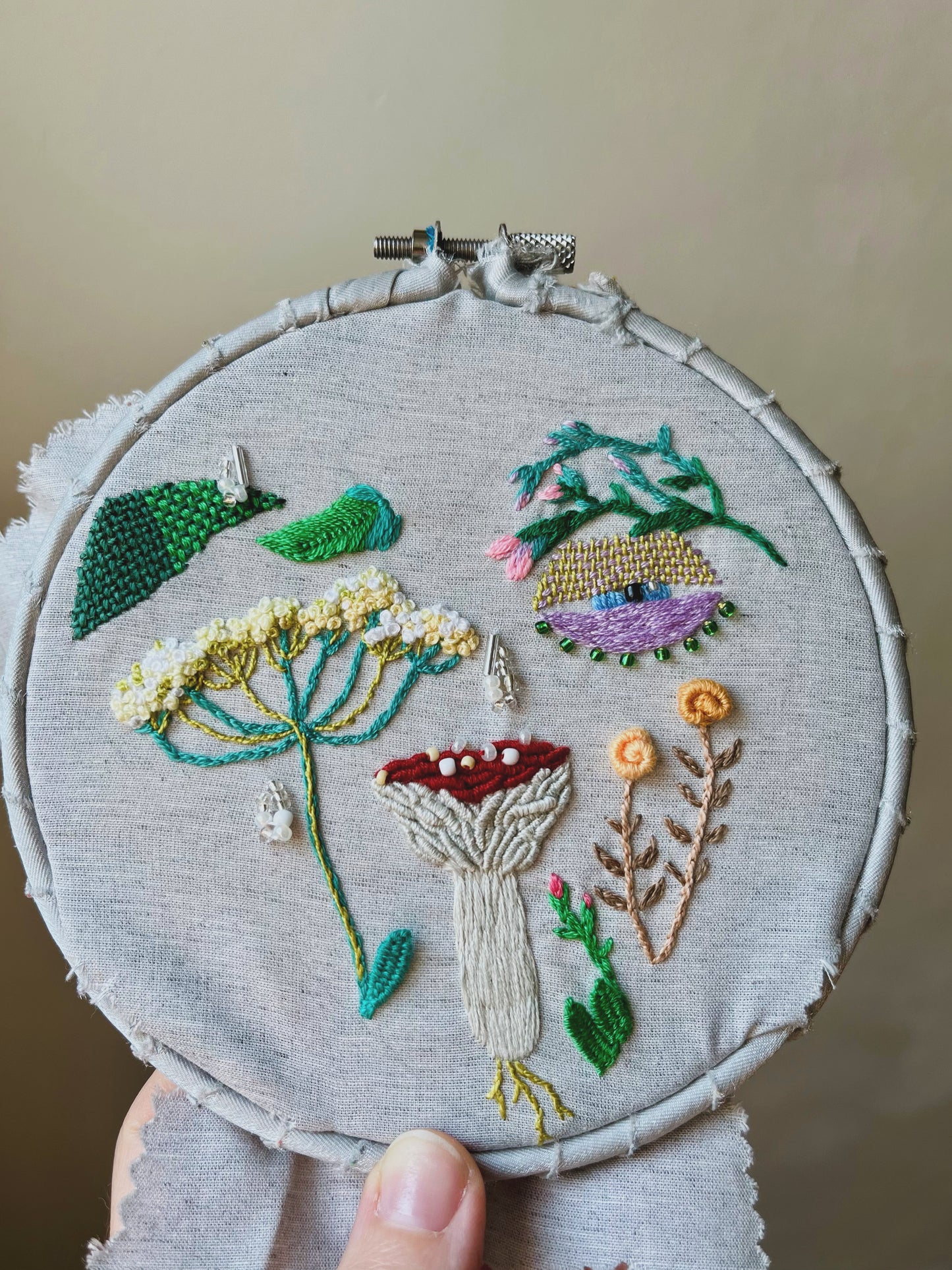Embroidery hoop with mushroom and wildflowers-themed design on a neutral background