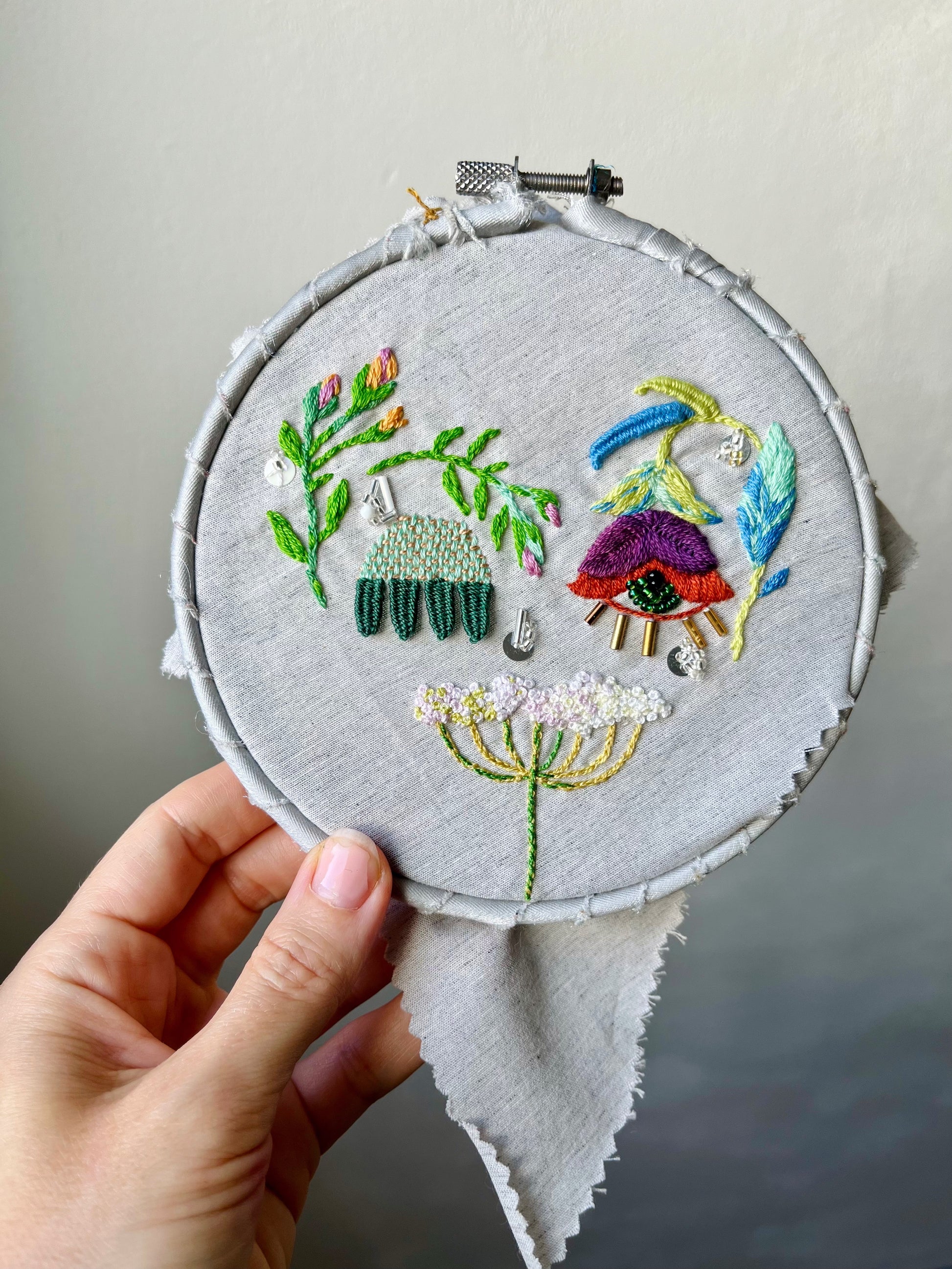 Embroidery hoop with mystical eyes and queen's lace design held by a hand against a neutral background