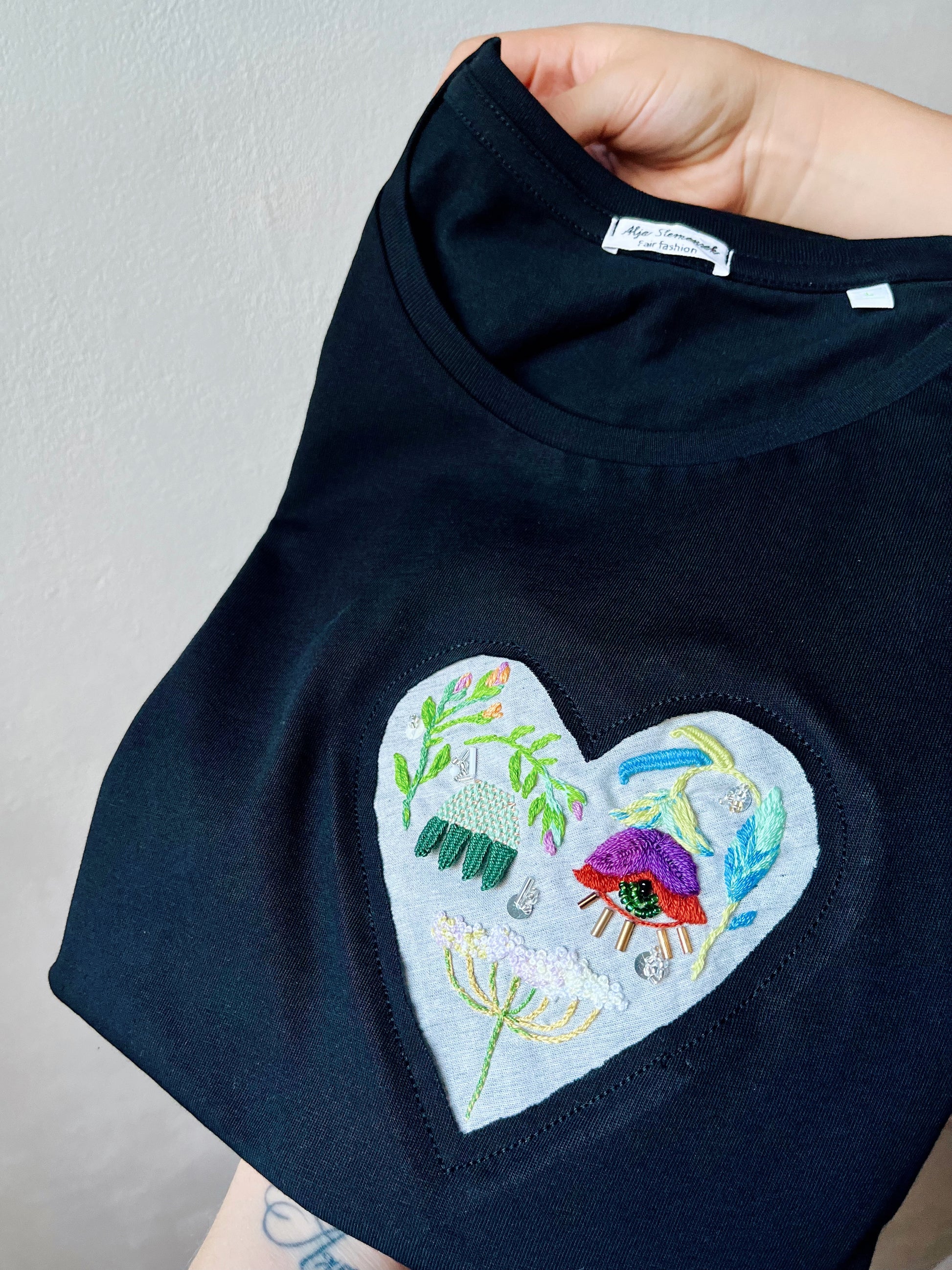 Black t-shirt with a colorful embroidered heart design featuring mystical eyes and queen's lace