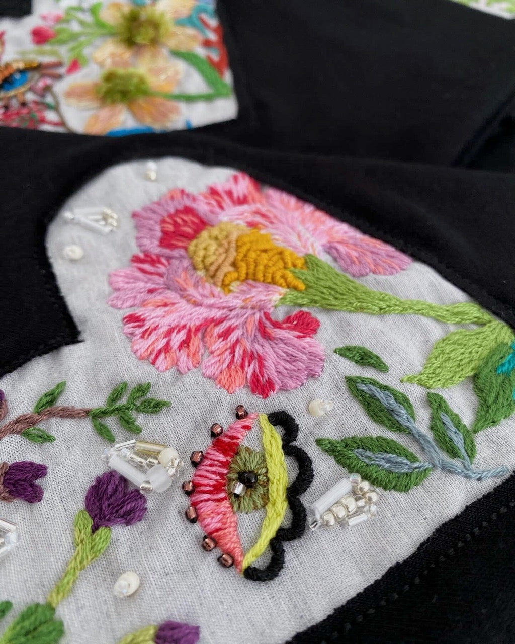 Close-up of an embroidered wild rose design on a black t-shirt with mystical eye and green leaves.