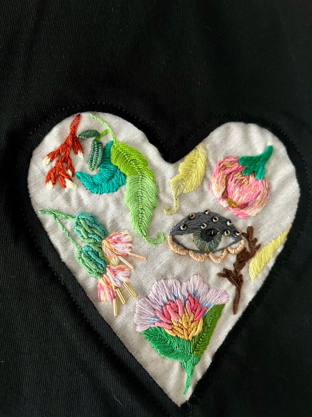 Close-up of a heart-shaped embroidery with wildflowers and leaves design on a black t-shirt.