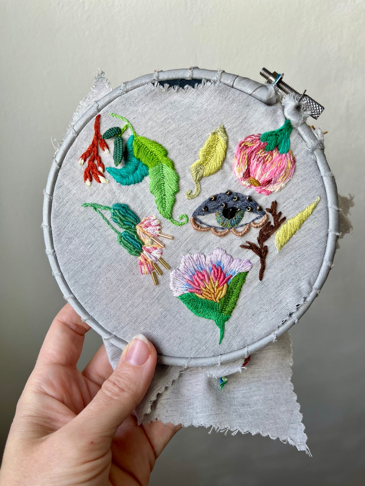 Embroidery hoop with wildflowers and leaves held by a hand against a neutral background