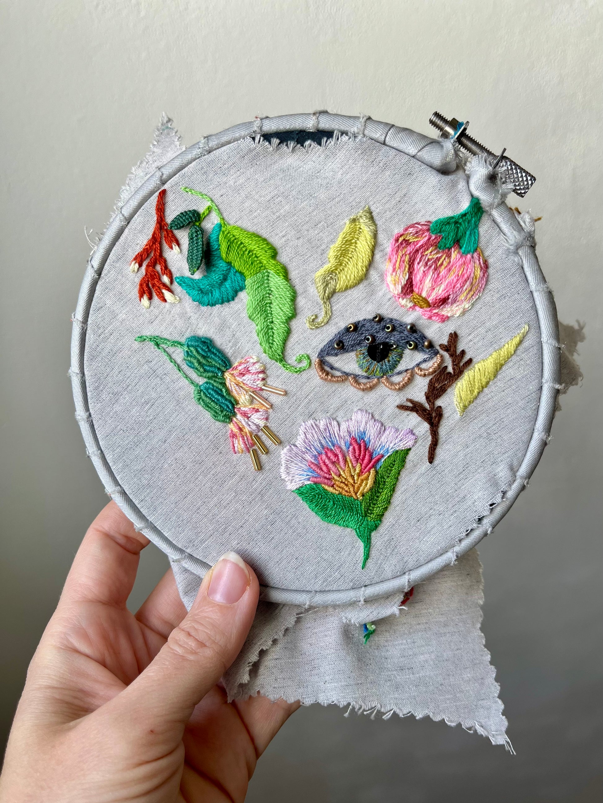 Embroidery hoop with wildflowers and leaves held by a hand against a neutral background