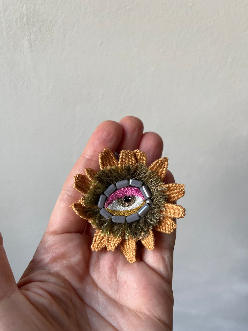 Hand-embroidered eye flower brooch with grey glass beads and woven petals, handmade in Vienna