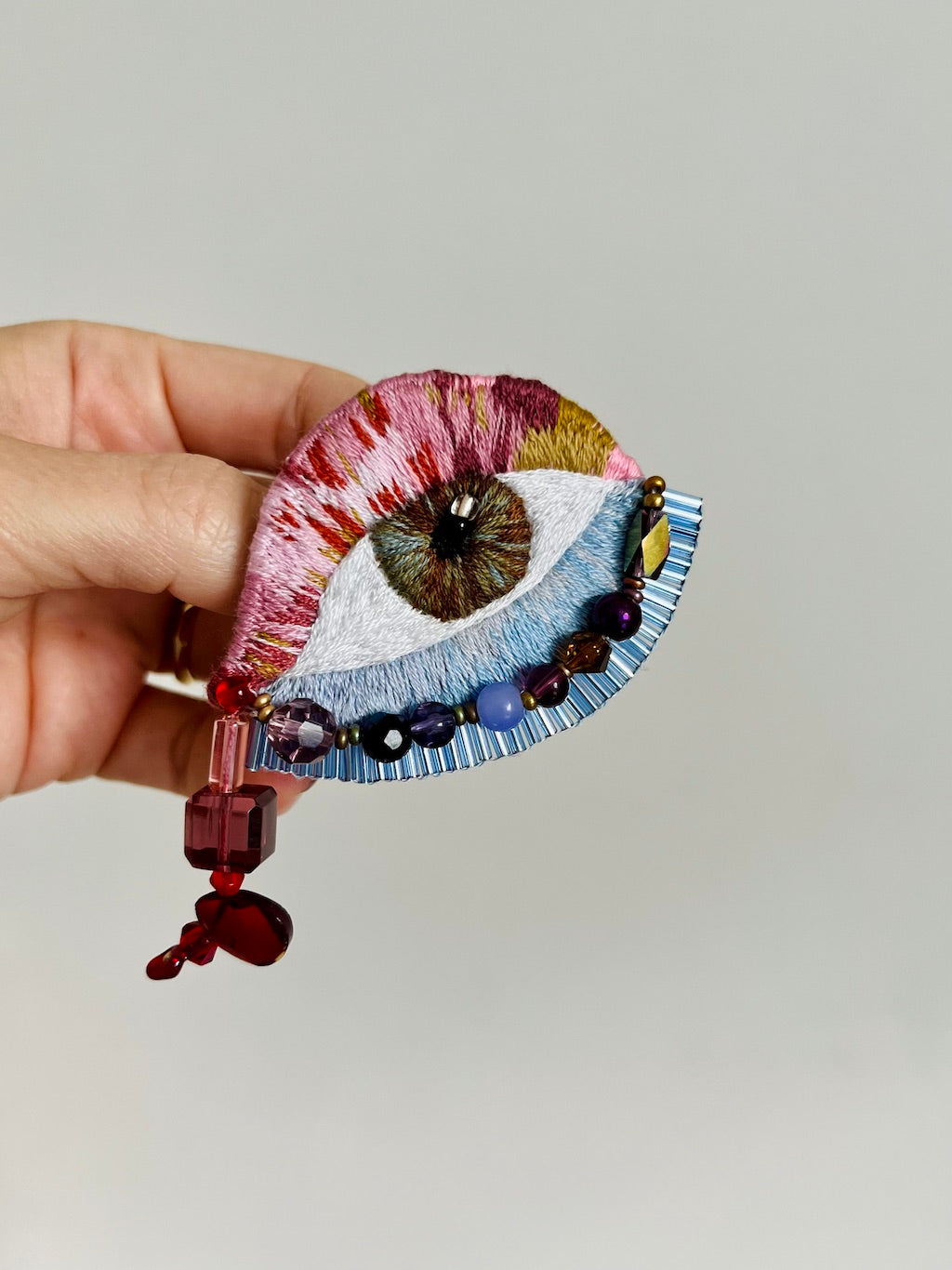 Hand holding a decorative brooch with beads against a plain background